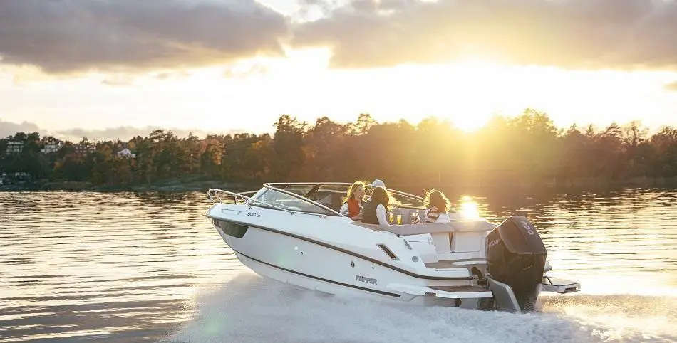 A white motorboat speeds across a calm lake at sunset, with four people enjoying the ride.